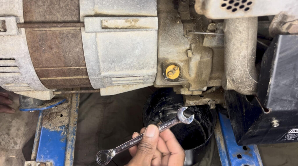 Using a 7/16 inch wrench to remove a generator oil drain plug.