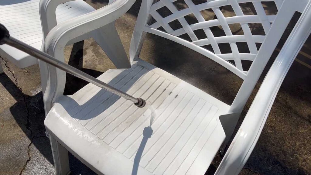 Using a Greenworks pressure washer wand to clean outdoor patio furniture.