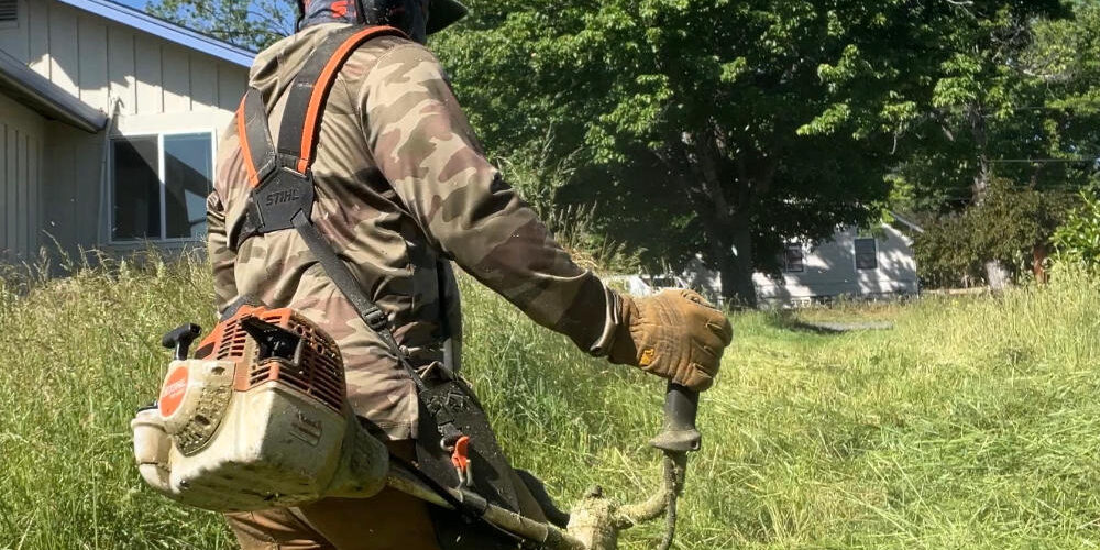 Man cutting over grown yard with commercial string trimmer